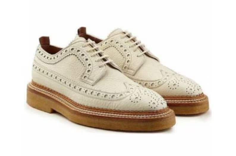 Pair of cream-colored brogue shoes with brown soles on a white background