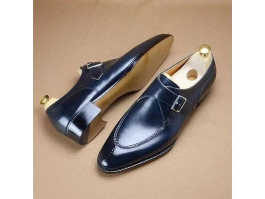 Pair of navy blue leather shoes with gold buckles on a beige background