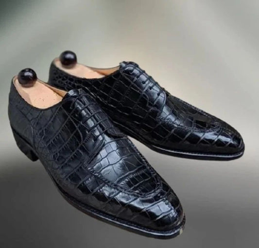 Black crocodile-patterned dress shoes on a gray background