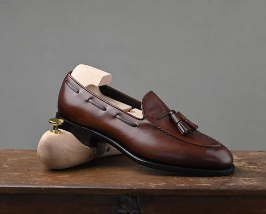 Brown leather loafer with tassel on a wooden surface and gray background