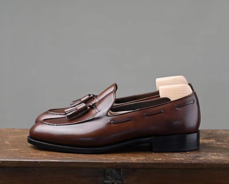 Brown leather loafer with tassel on a wooden surface and gray background