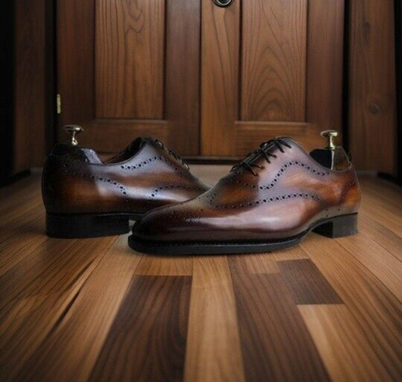 Pair of brown leather dress shoes on a wooden floor with a wooden door in the background.