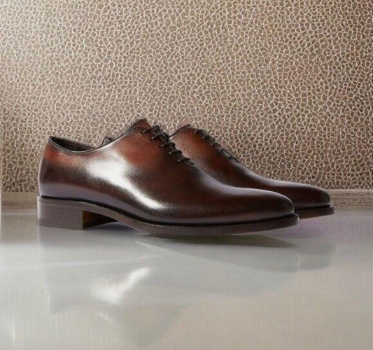 Pair of brown leather shoes on a reflective surface with a patterned wall in the background