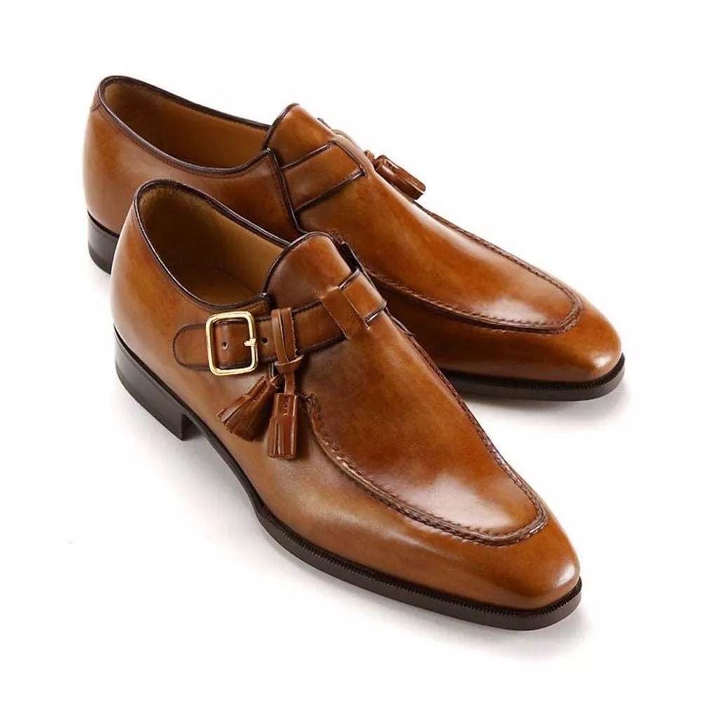 Pair of tan leather shoes with buckles and tassels on a white background