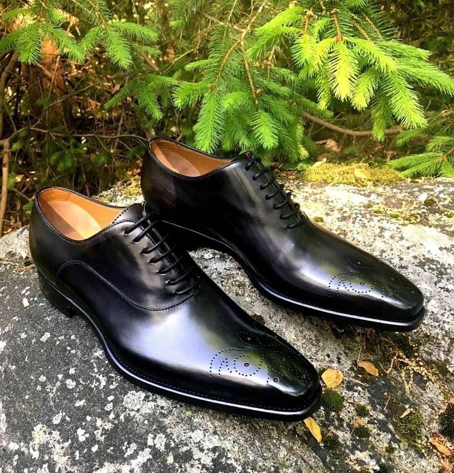 Pair of black dress shoes on a stone surface with green foliage in the background