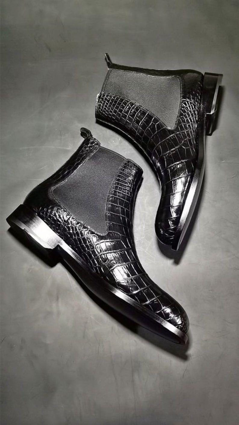 Black crocodile-patterned boots on a gray surface