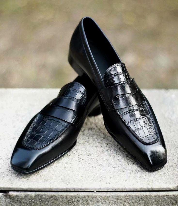 Black leather loafers with crocodile texture on a stone surface
