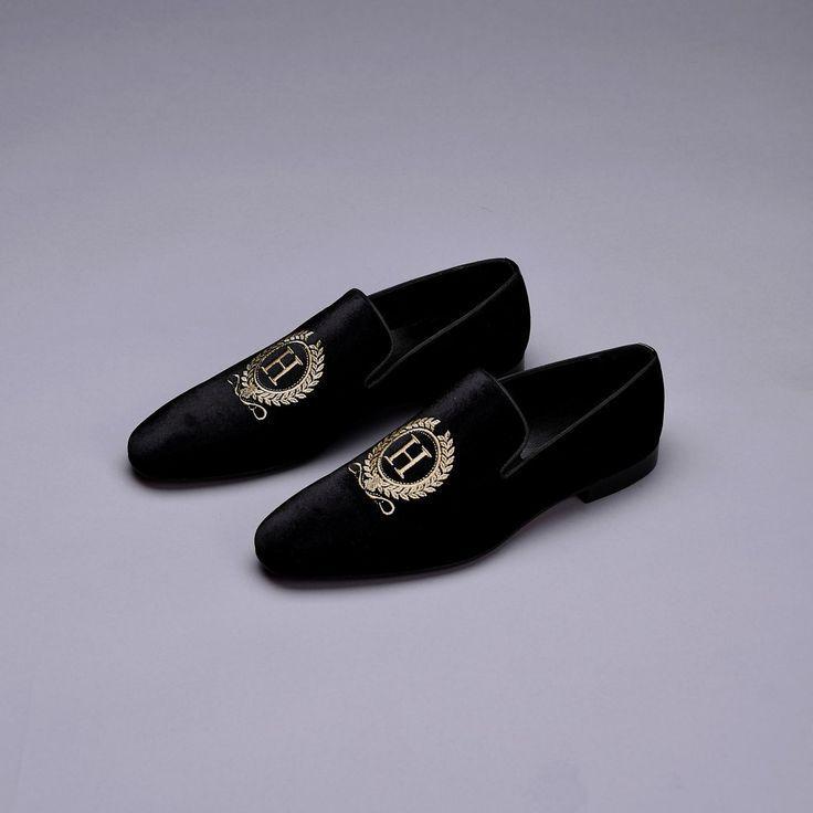 Pair of black velvet loafers with gold embroidery on a gray background