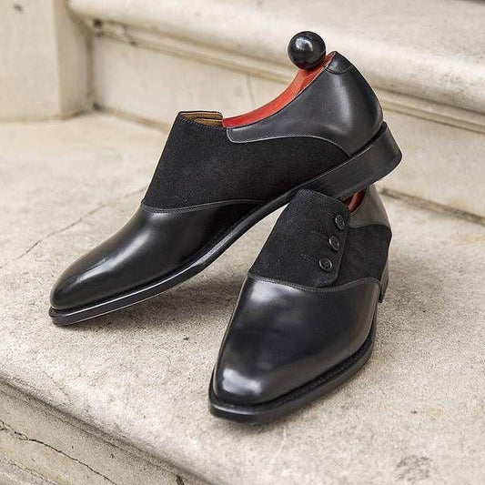 Pair of black dress shoes with a side button closure on a stone surface