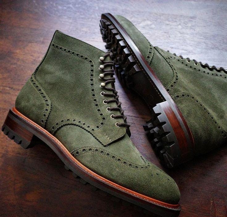 Green suede shoes with brown soles on a wooden surface