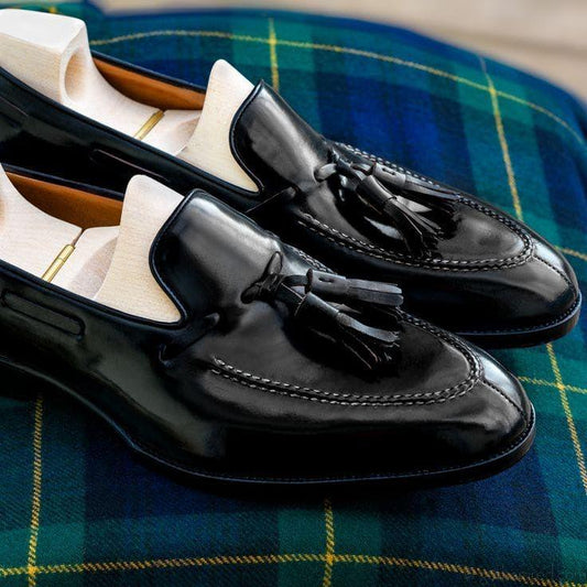 Black loafers with tassels on a plaid fabric background