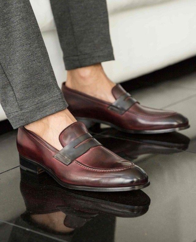 Burgundy loafers worn with gray pants on a reflective surface