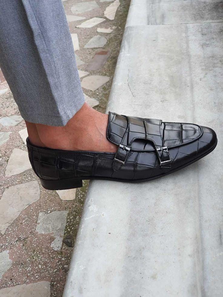 Black crocodile-patterned loafers worn on a stone pavement.