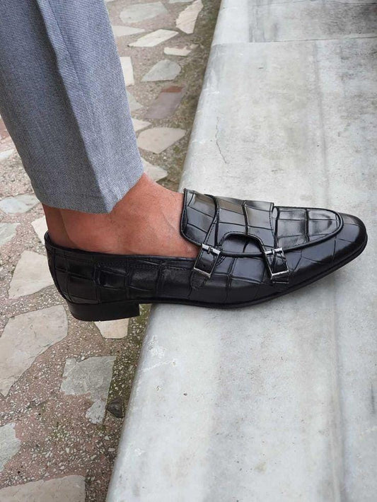 Black crocodile-patterned loafers worn on a stone pavement.