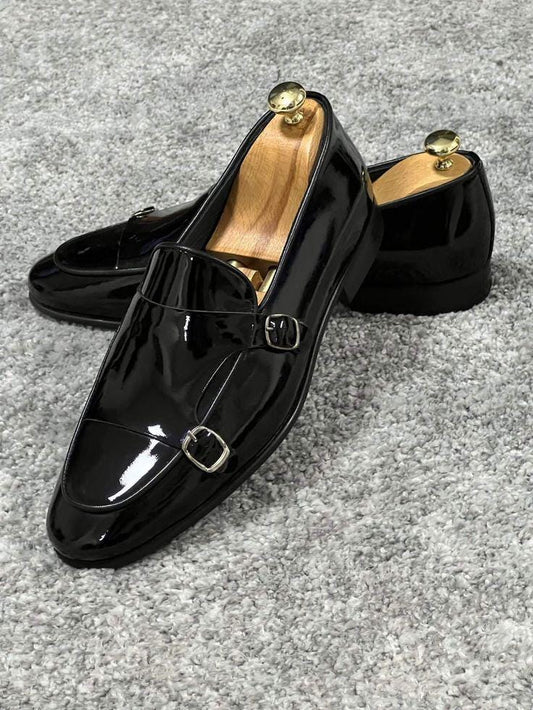Black glossy loafers with buckles on a gray surface
