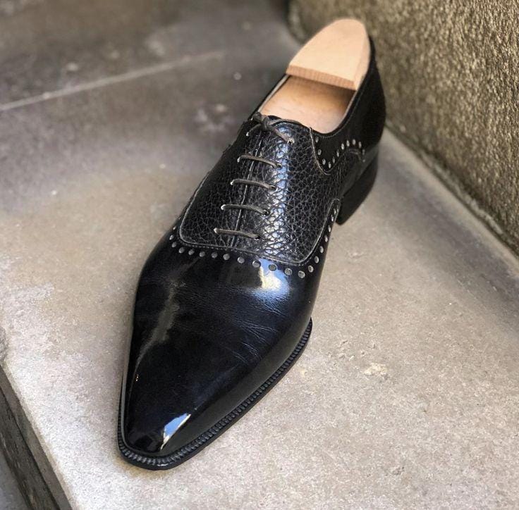 Black dress shoe with a pointed toe on a concrete floor