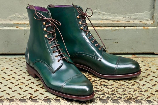 Pair of green leather boots with brown laces on a textured surface.