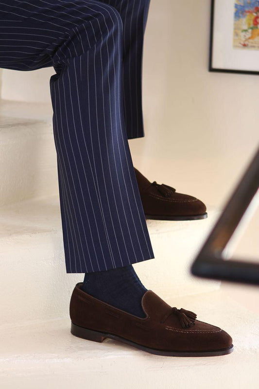 Person wearing navy pinstripe pants and brown tassel loafers on a light background
